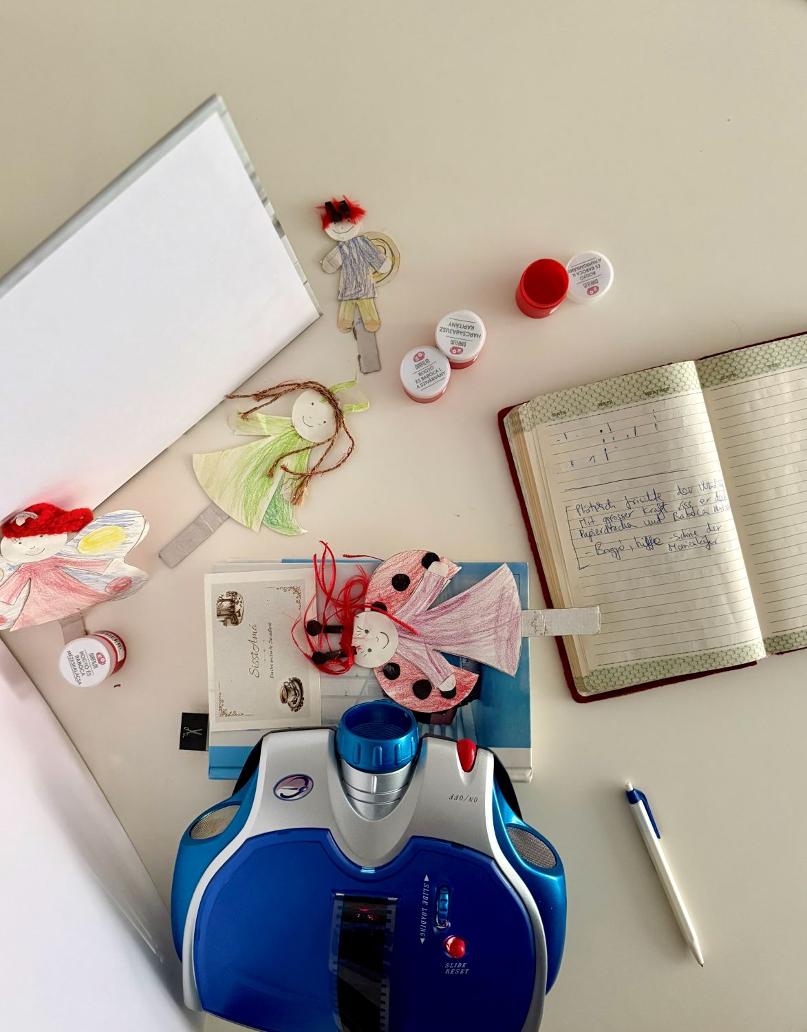 Tisch von oben mit gebastelten Figuren, Diafilm-Döschen, Notizbuch und Diaprojektor