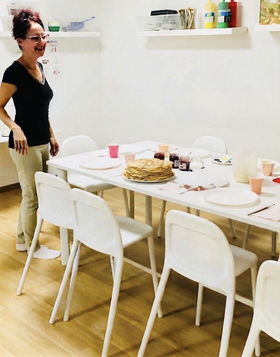 Andrea steht lachend neben dem gedeckten Tisch mit einem Stapel Palatschinken in der Mitte