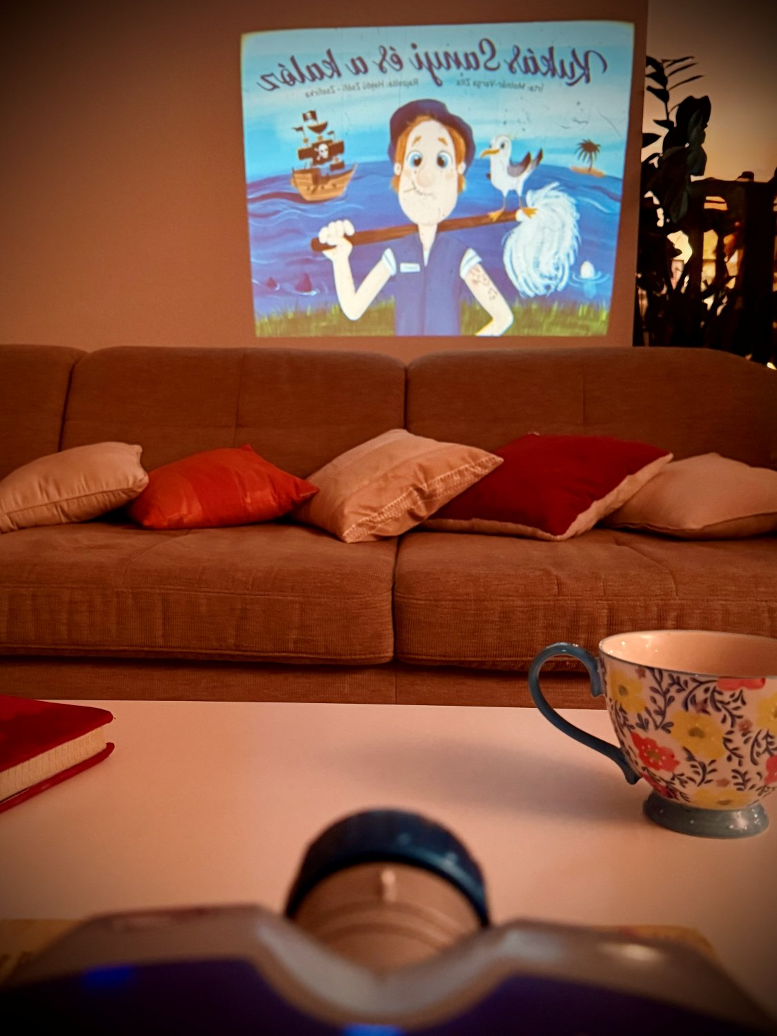 Diaprojektor im Vordergrund, dahinter ein Sofa mit Kissen und das Märchenbild an der Wand